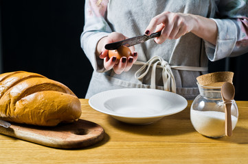 Chef breaks a chicken egg over a plate. The concept of cooking French toast. Black background, side view, space for text, kitchen