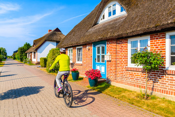 Young woman riding bike in Moritzdorf village with typical red brick house with straw roof along...
