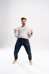 Happy winner. Full length portrait of happy young handsome man gesturing and keeping mouth open while standing against white background.