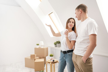 A young married couple, a man and a woman, in a new white, bright apartment, against the background of boxes with things, are discussing the renovation and layout of the house.