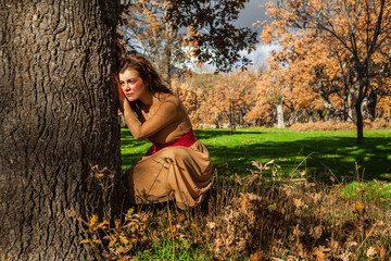 Portrait full shot elegant young woman crouch in the ground. Tree. Thoughtful. In love. Autumn
