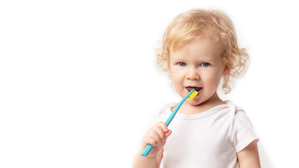 Caucasian little cute curly baby girl in white clothes body brushing her teeth with a colored blue brush on a white background.