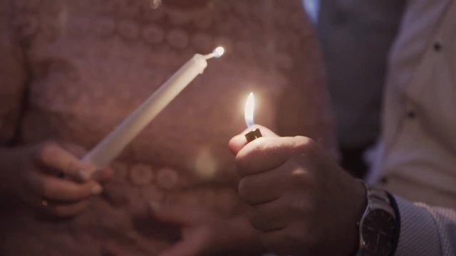 A man lighter lights a candle in the hands of a woman.