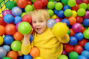 Fototapeta na wymiar Happy little boy having fun in ball pit with colorful balls. Child playing on indoor playground.