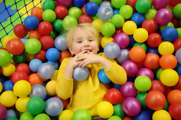 Fototapeta na wymiar Happy little boy having fun in ball pit with colorful balls. Child playing on indoor playground.