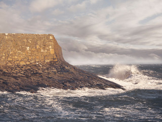 Wave about to crash on a harbour's water braker. Dramatic sky, Warm wall and cold water colors.