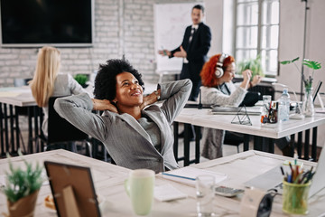 Happy black businesswoman with hands behind head day dreaming in the office.