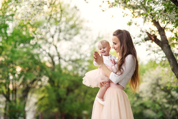 Obraz premium Mother holds her little daughter in her arms among blooming trees. Mom and her little baby weared pink family look dress.