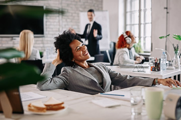 Happy African American businesswoman taking a break and day dreaming at her office desk.