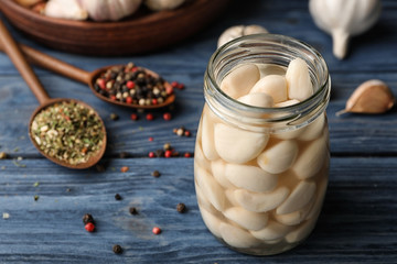 Preserved garlic in glass jar on wooden table. Space for text