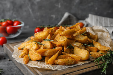 Wooden board with baked potatoes and rosemary on table