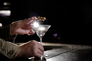 Barman adding olives to martini cocktail on counter, closeup. Space for text