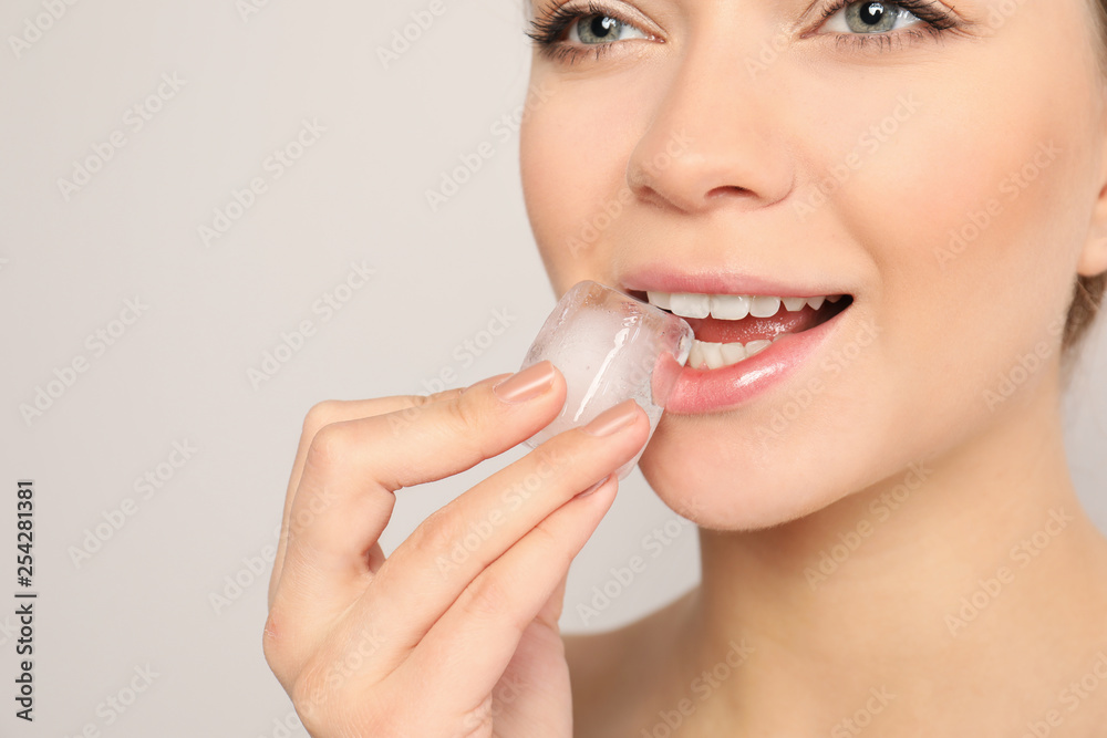 Wall mural Young woman with ice cube on light background