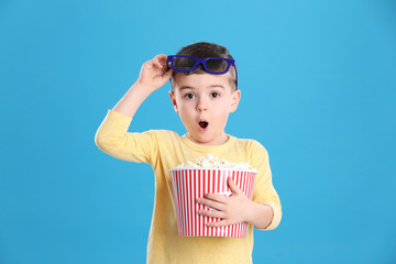 Cute little boy with popcorn and glasses on color background