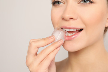 Young woman with ice cube on light background