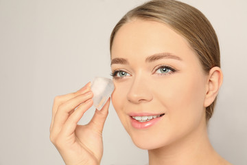 Young woman with ice cube on light background. Skin care