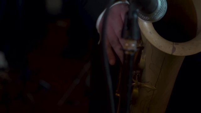 Saxophone player plays into microphone at the live event, wedding ring can be seen on his hand.