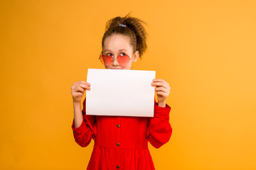 girl holding white sheet.Cute little girl with white sheet of paper.yellow background.copy spase.Little girl holding empty sheet of a paper