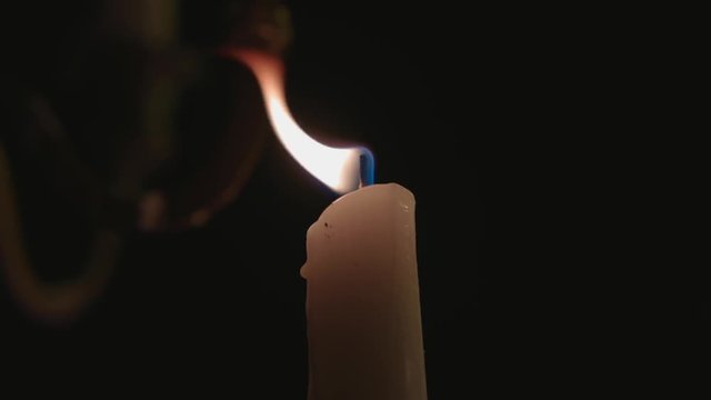 A lone white candle being lite by another candle.
