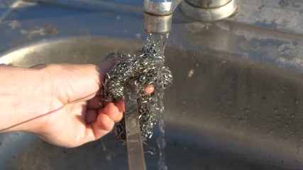 Long metallic skewer is washed with a fluffy metallic wisp outdoors in slo-mo