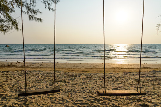 Silhouette scenery of double wooden swings hang from a tree on a beach and background of sea, skyline and sunset without people. Lonely vacation with nobody on the beach before sunset.