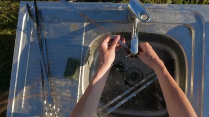 Female hands rubbing long skewers with a metallic wisp outdoors in slo-mo