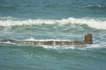 Small waves are washing over a rock shelf in the ocean. The rocks are brown and nearly fully submerged. The water is blue, and fills the photo.