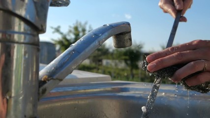 Female hands washing a lengthy skewer over a garden sink in summer in slo-mo