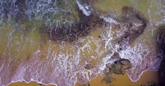 4K fly over palm trees , beach and into the ocean over waves crashing on shore and rocks.