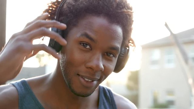 African American man looking into camera and putting on headphones.  Sun flare.
