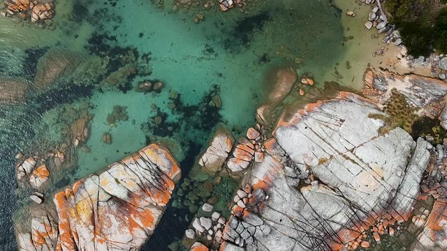 Aerial of Bay of Fires bright orange rocks with waves in rock pools in the sea. Binalong Bay, Tasmania, Australia