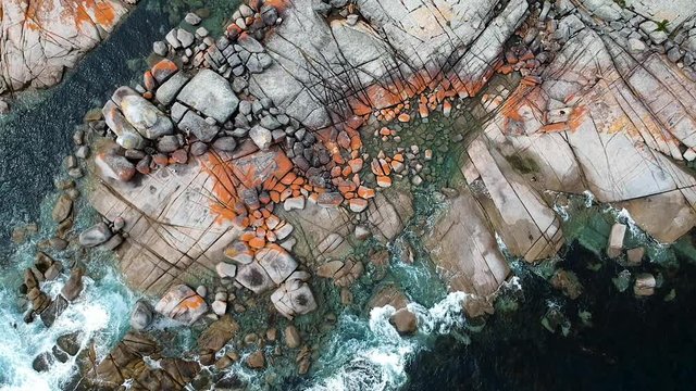 Aerial of Bay of Fires bright orange rocks with waves in rock pools in the sea. Binalong Bay, Tasmania, Australia