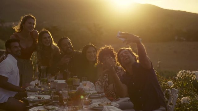 Man with friends taking selfie with his smart phone. Group selfie at outdoor dinner party.