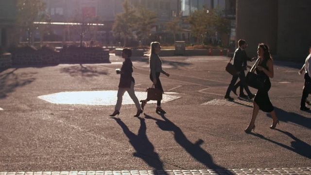 Business people commuting on a busy city street early in the morning. Commuters walking on a city street going to office. Zoom out shot.
