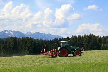 Im Sommer mäht ein Bauer mit seinem Traktor in Bayern Gras