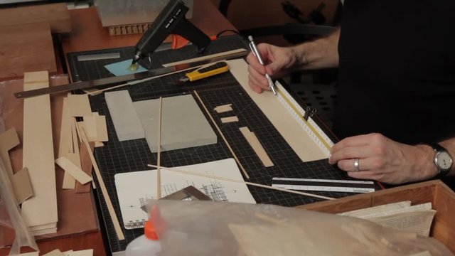 Close up view of male architect's hand's cutting wood strips in a design studio on a worktable to assemble a scale model of a house project.
