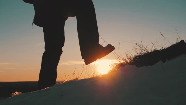 Hiker walking outdoors at sunset on the rock. Legs in trekking boots go along the mountain ridge against the backdrop of the sun Close up of leg walking in slow motion. Travel and adventure concept.