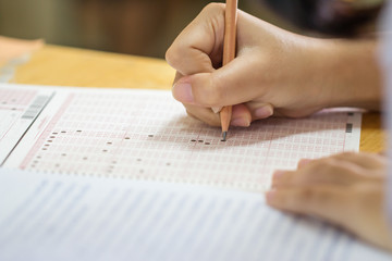 Student taking exams, writing examination on paper answer sheet optical form of standardized test...