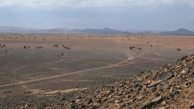 Pickup truck driving through an hot desert vally in the Sahara, Morocco. Handheld zoomed in shot.