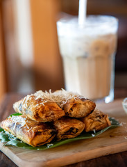 Fried banana  with cheese on the top of banana leaf and wooden cutting board. Selective focus with blur glass of coffee milk on background.