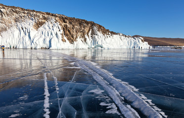 Tourists rest in the winter on Lake Baikal on a sunny day off and take pictures of icicles and ice crusts on the rocks of Hubyn Island