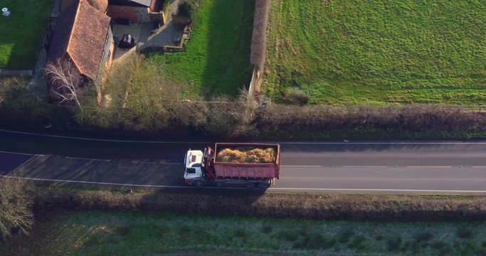 Aerial view tracking an unrecognizable lorry (HGV Truck) along a road carrying agricultural materials.