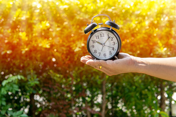 The man holding alarm clock in sunlight and park background show concept of giving time or dividing...