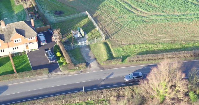 Aerial tracking shot of a SUV 4X4 vehicle driving along a country road into a village.