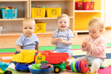 Nursery babies girl and boys playing together in playroom in kindergarten