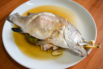 Cooking sea bass fish steamed with sauce and herb ingredient on white plate