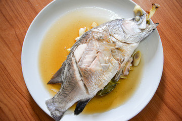 Cooking sea bass fish steamed with sauce and herb ingredient on white plate