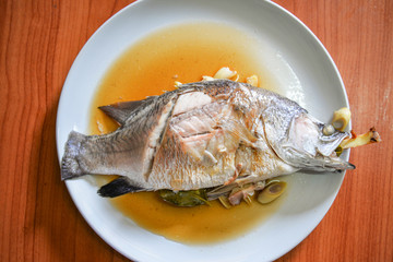 Cooking sea bass fish steamed with sauce and herb ingredient on white plate