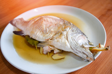 Cooking sea bass fish steamed with sauce and herb ingredient on white plate