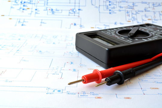 measuring device electric tester with red and black probe on background of large sheet of paper with drawn color electrical circuit